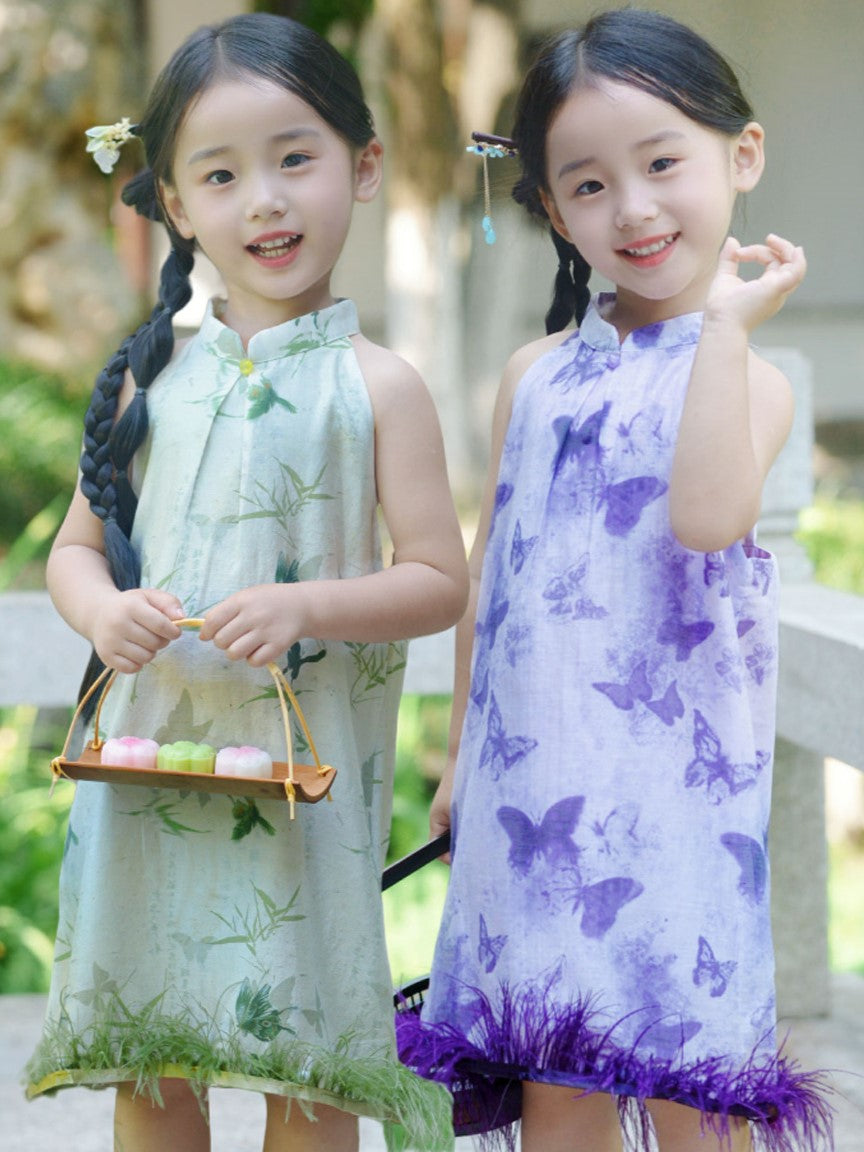 Two girls wearing traditional cheongsam dresses with butterfly and ostrich feather patterns, one in purple and the other in green, holding a small basket.