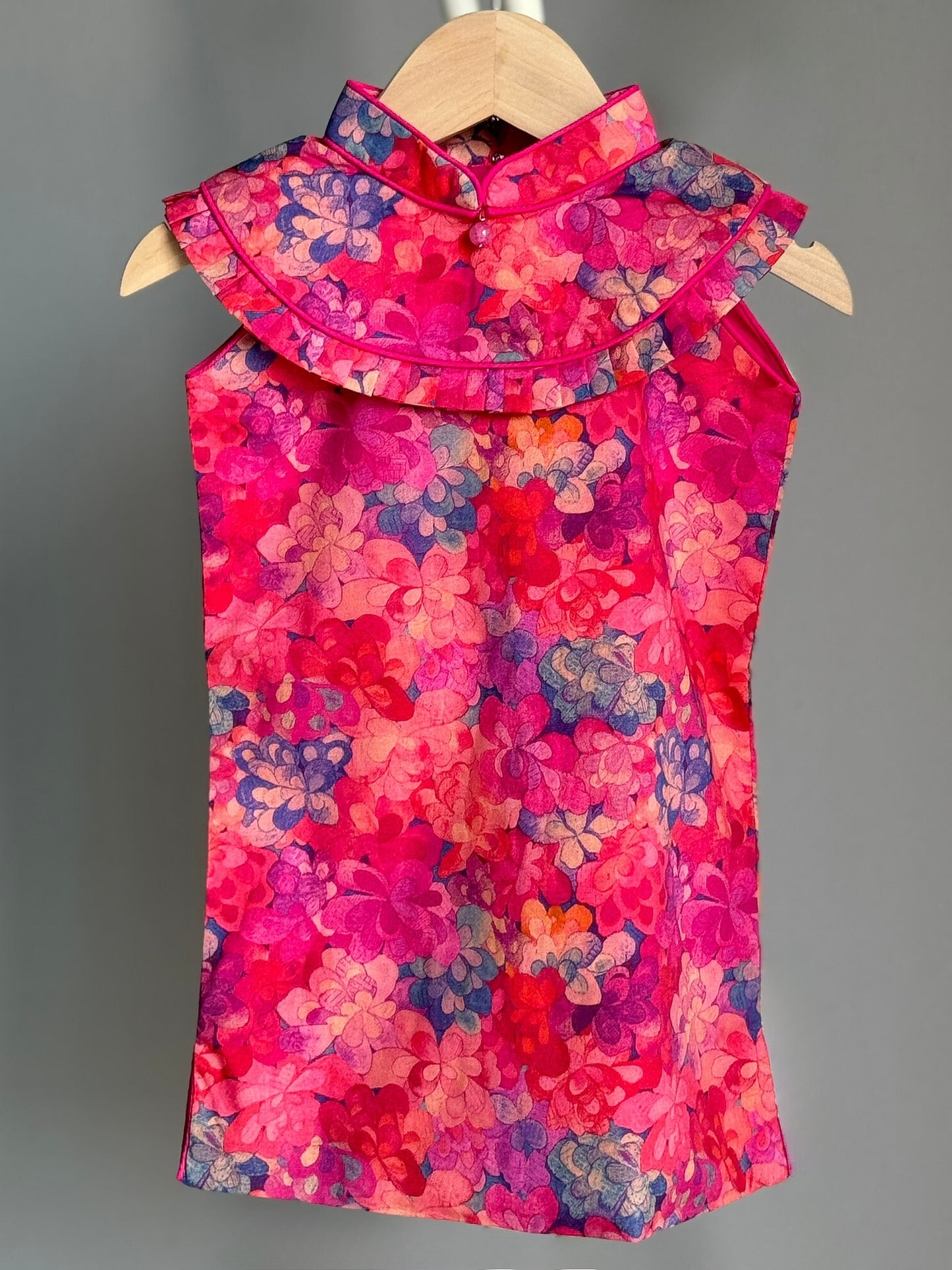 A red and pink floral print cheongsam dress for girls, displayed on a wooden hanger.