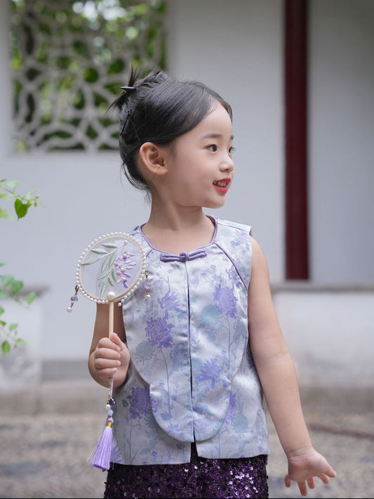 Young girl in a floral dress holding a decorative fan outdoors.