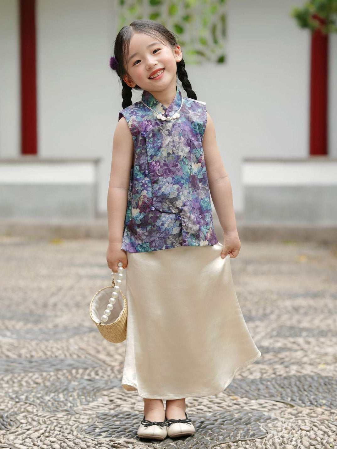 Young girl in a floral top and beige skirt standing in a traditional setting.